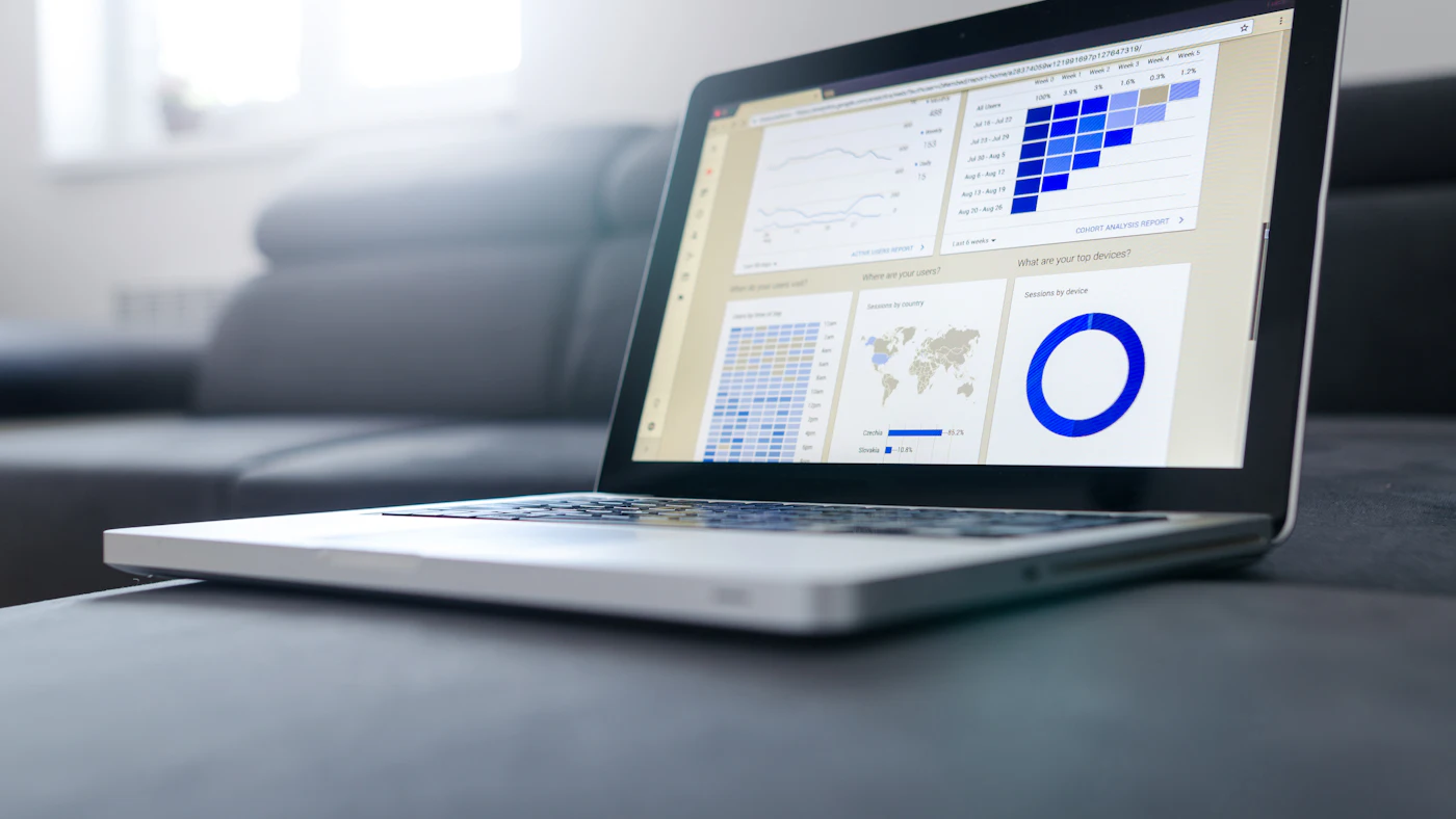 Laptop menampilkan dashboard berisi grafik dan tabel laporan
