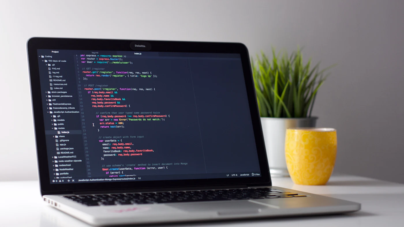 Laptop di atas meja menampilkan kode program dan jendela terminal