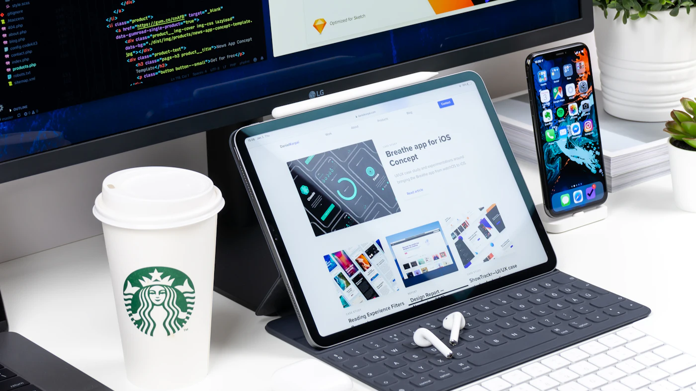 Meja kerja dengan monitor, tablet, dan ponsel yang menampilkan rancangan halaman web