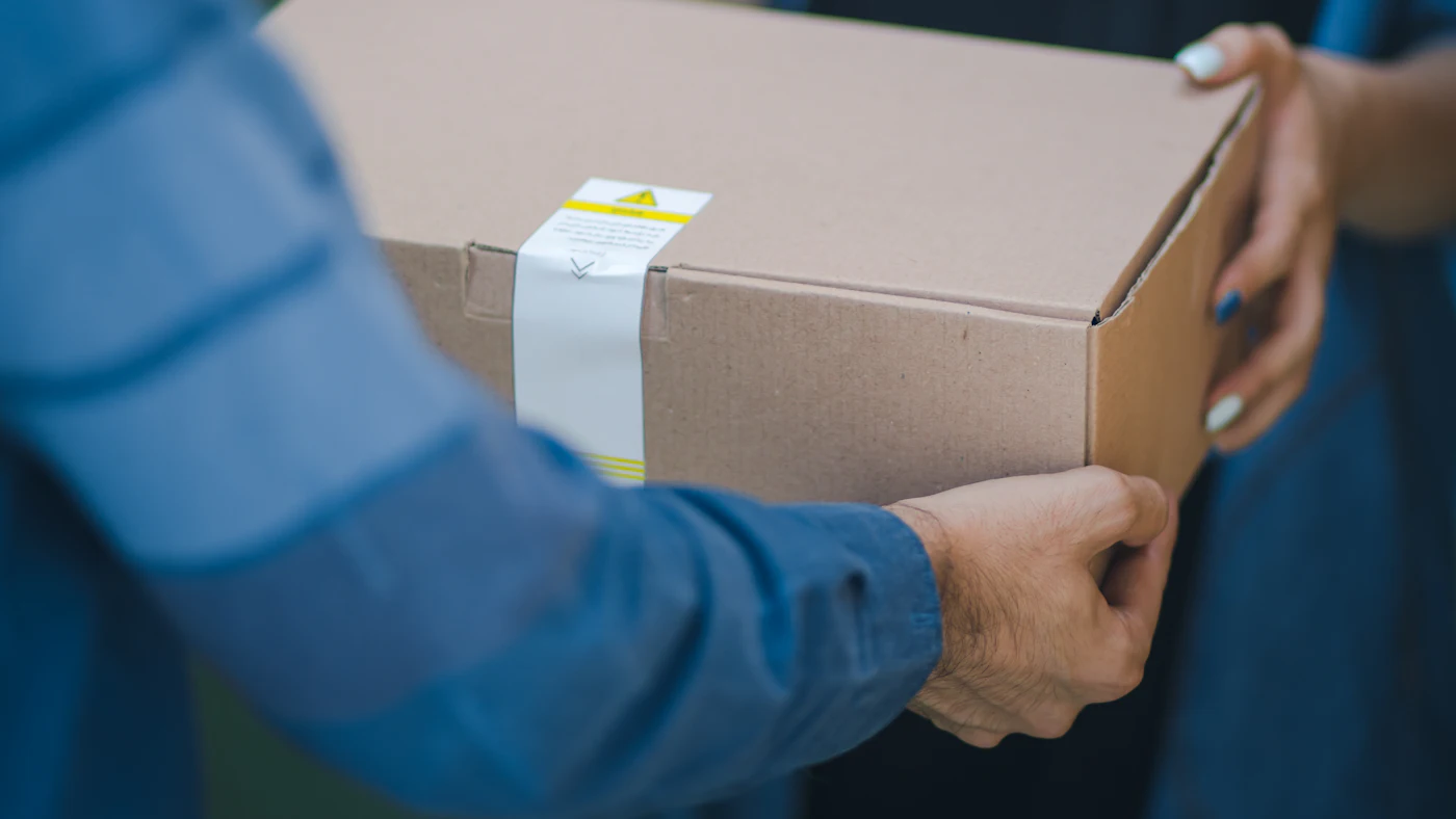 Dua orang menyerahkan sebuah paket kardus yang sudah dilakban