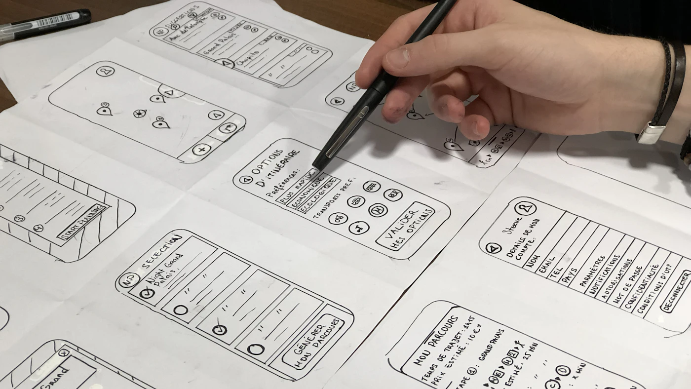 Tangan menggambar sketsa wireframe beberapa layar aplikasi di atas kertas