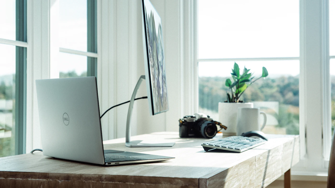 Laptop dan monitor di meja dekat jendela besar